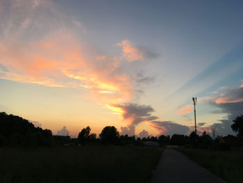 Road by silhouette trees against sky during sunset