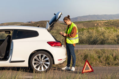 Young man texting his family on the phone to get safe him from the side of the road with broken car