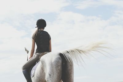 Woman riding horse against cloudy sky