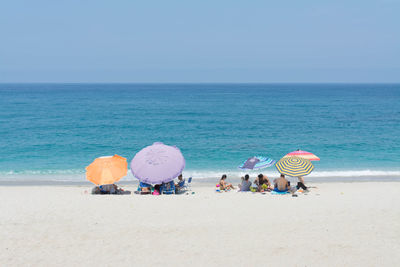 People at beach against clear blue sky