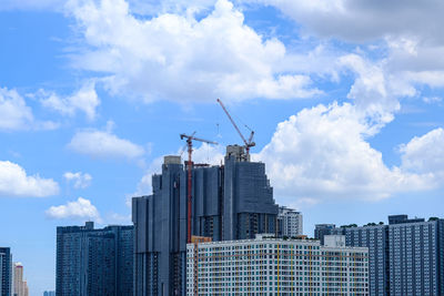 Low angle view of crane by buildings against sky