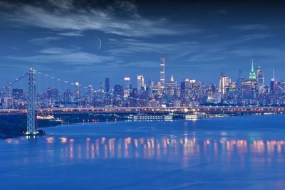 Illuminated buildings by river against sky at night