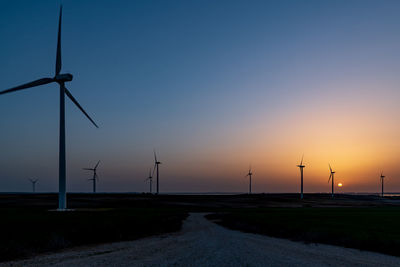 Wind turbines on field against sky during sunset