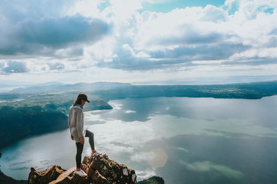 Woman standing on cliff by sea against sky