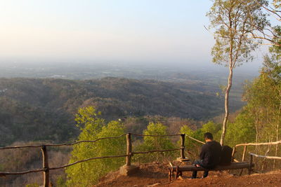 Rear view of man sitting on landscape against mountains