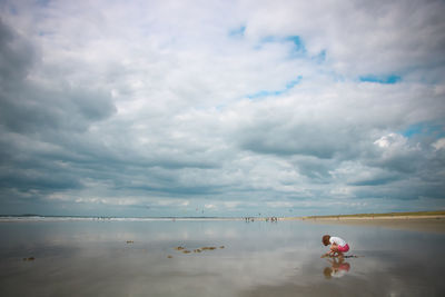 Girl digging sand at beach against cloudy sky