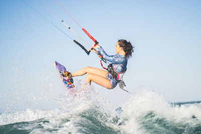 Side view of fit female kite surfer in swimsuit ridding waves in sea on sunny day in summer