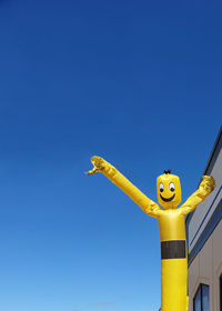 Low angle view of yellow sculpture against clear blue sky