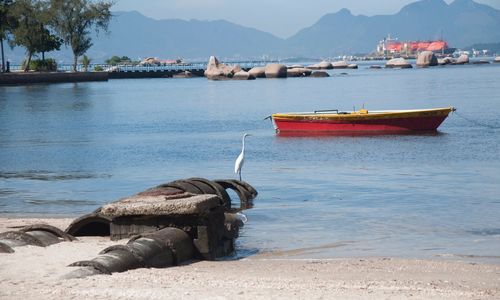 Boat moored on sea by mountain against sky