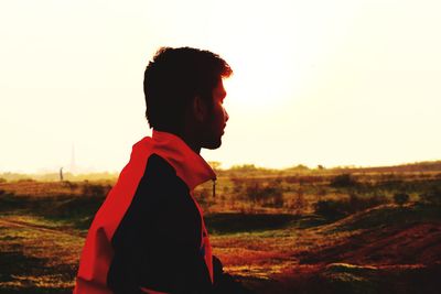 Side view of man standing on field against sky during sunset
