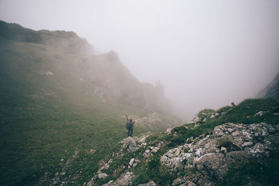 Woman standing on mountain against sky during foggy weather