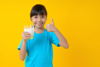 Portrait of smiling girl holding drink against yellow background