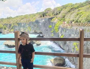 Boy standing by railing against sea