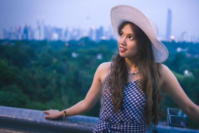 Beautiful young woman in hat standing against blurred background