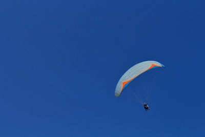 Low angle view of people paragliding against clear blue sky