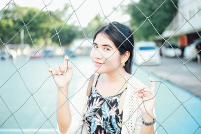 Portrait of young woman standing behind chainlink fence