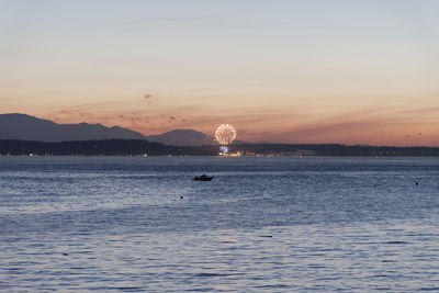 Sunset on the 4th of july with fireworks in the distance over water.