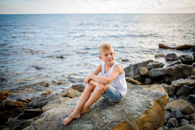 Young woman sitting on rock at sea shore against sky