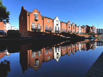 Reflection of buildings in lake against clear blue sky