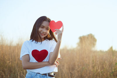 Woman holding heart shape while standing on field