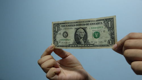 Cropped hands of woman holding paper currency against wall