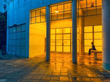 Man walking on illuminated footpath by building at night