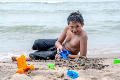 A handsome young boy is digging in the sand and using molds to create sand castles
