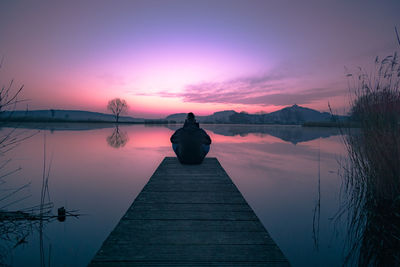 Rear view of man on pier over lake against sky during sunset