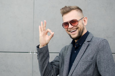 Portrait of cheerful man gesturing while standing against wall