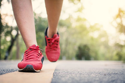 Low section of woman walking on road against trees