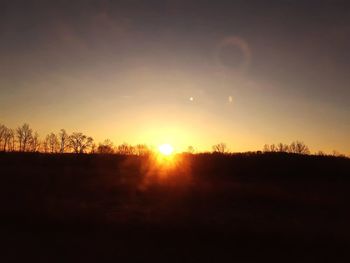 Silhouette trees on field against sky during sunset