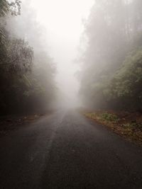 Empty road by trees against sky