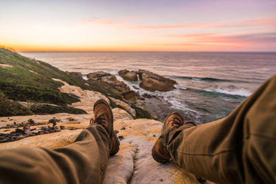Low section of people relaxing on shore against sunset sky