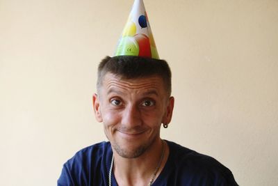 Portrait of man smiling while wearing party hat against wall