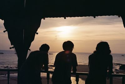 Silhouette people overlooking calm sea at sunset