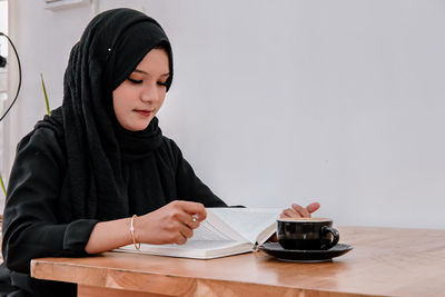 Portrait of young woman reading book at table