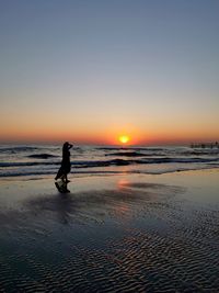 Silhouette man on beach against sky during sunset