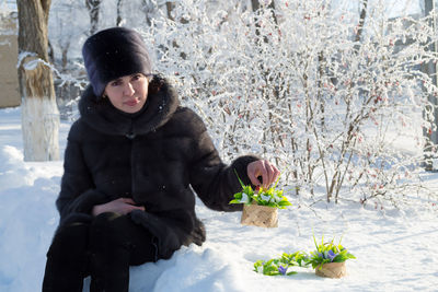 A woman in a mink fur coat and a hat sitting on the snow with smile holds basket with handmade 