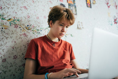 Teenage girl sitting on bed studying online using laptop.