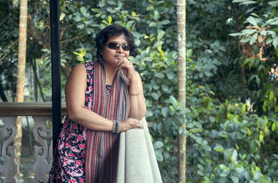 A young indian woman in sunglass and beautiful ethnic dress, enjoying view of garden from balcony
