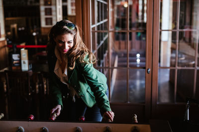 From above of joyful brown haired woman in stylish outfit laughing while playing table football in modern cafe