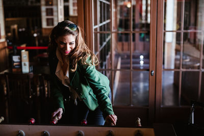 From above of joyful brown haired woman in stylish outfit laughing while playing table football in modern cafe