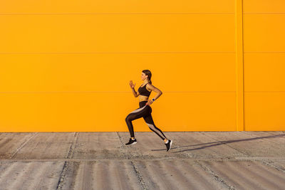 Full length of woman running on footpath against orange wall