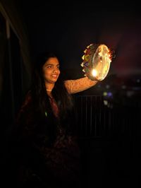 Portrait of young woman standing against illuminated chandelier