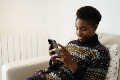 Young woman using smart phone while sitting on sofa at home