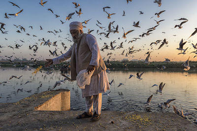 Man standing by lake against sky during sunset