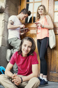 Portrait of teenage boy with friends in background at entrance of university