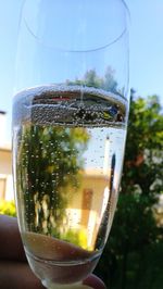 Close-up of hand holding glass of drink against sky