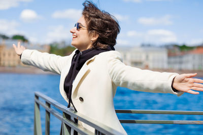 Beautiful young woman walks along embankment in white coat and black sweatshirt