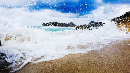 Waves reaching shore at beach against sky